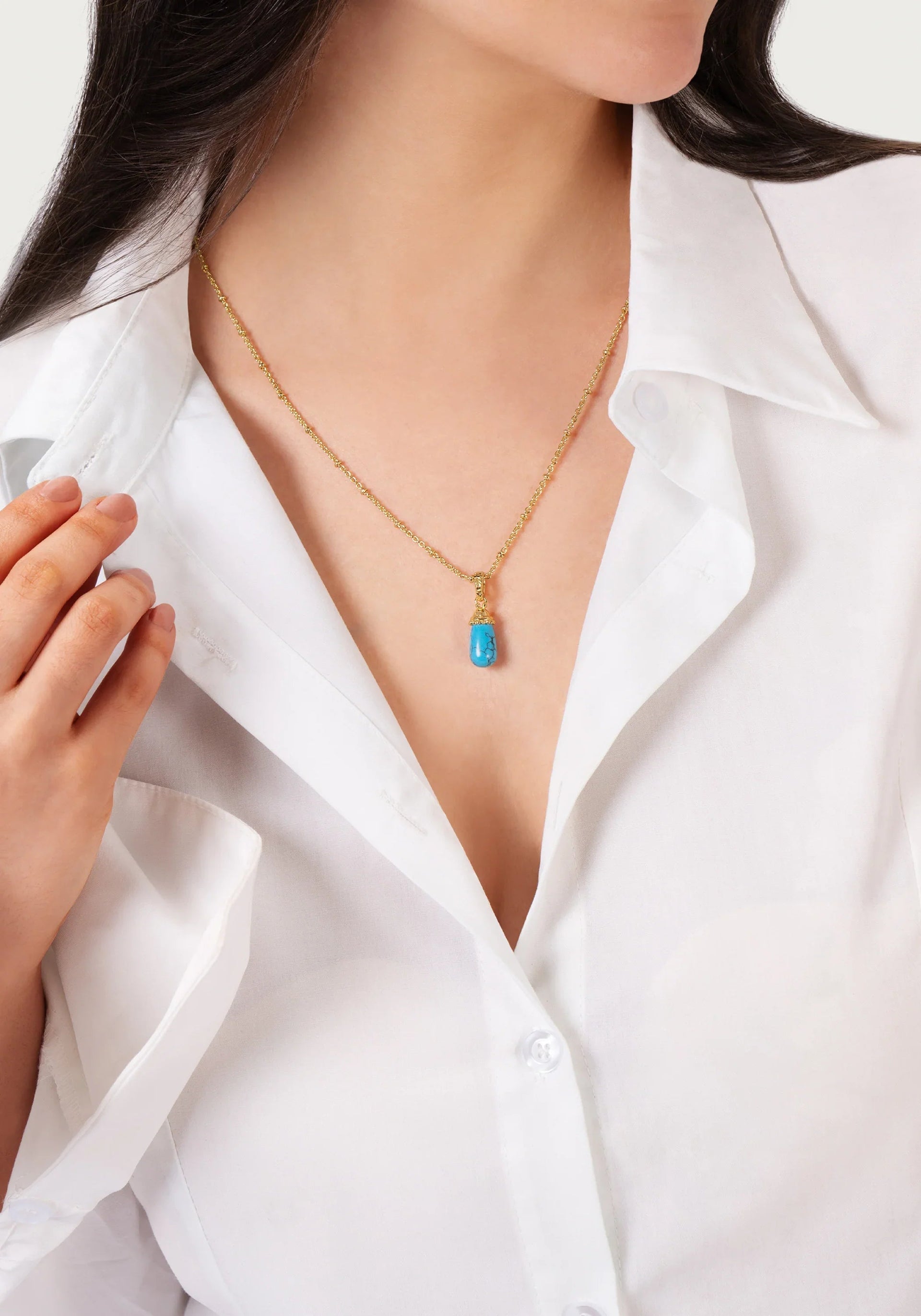 A woman wearing a white button-up shirt and the Anabel Aram Milos Stone Drop Charm necklace in turquoise.