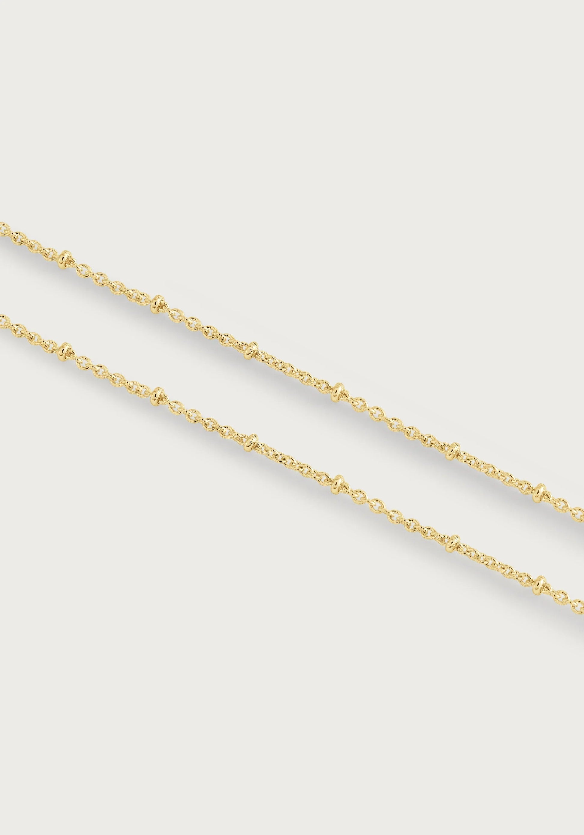 The Molten Bead Chain Necklace in gold by Anabel Aram features two thin molten chains with small, evenly spaced bead accents, displayed against a plain white background.