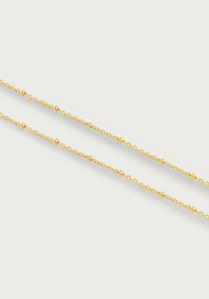 The Molten Bead Chain Necklace in gold by Anabel Aram features two thin molten chains with small, evenly spaced bead accents, displayed against a plain white background.
