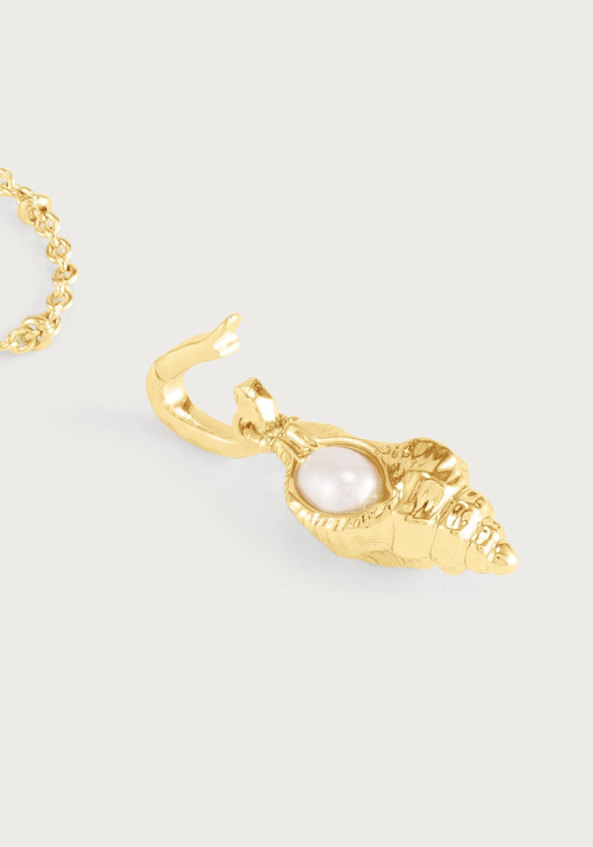 Anabel Aram Milos Shell with Pearl Charm, a gold shell-shaped pendant with a central pearl attached to a gold hoop earring.