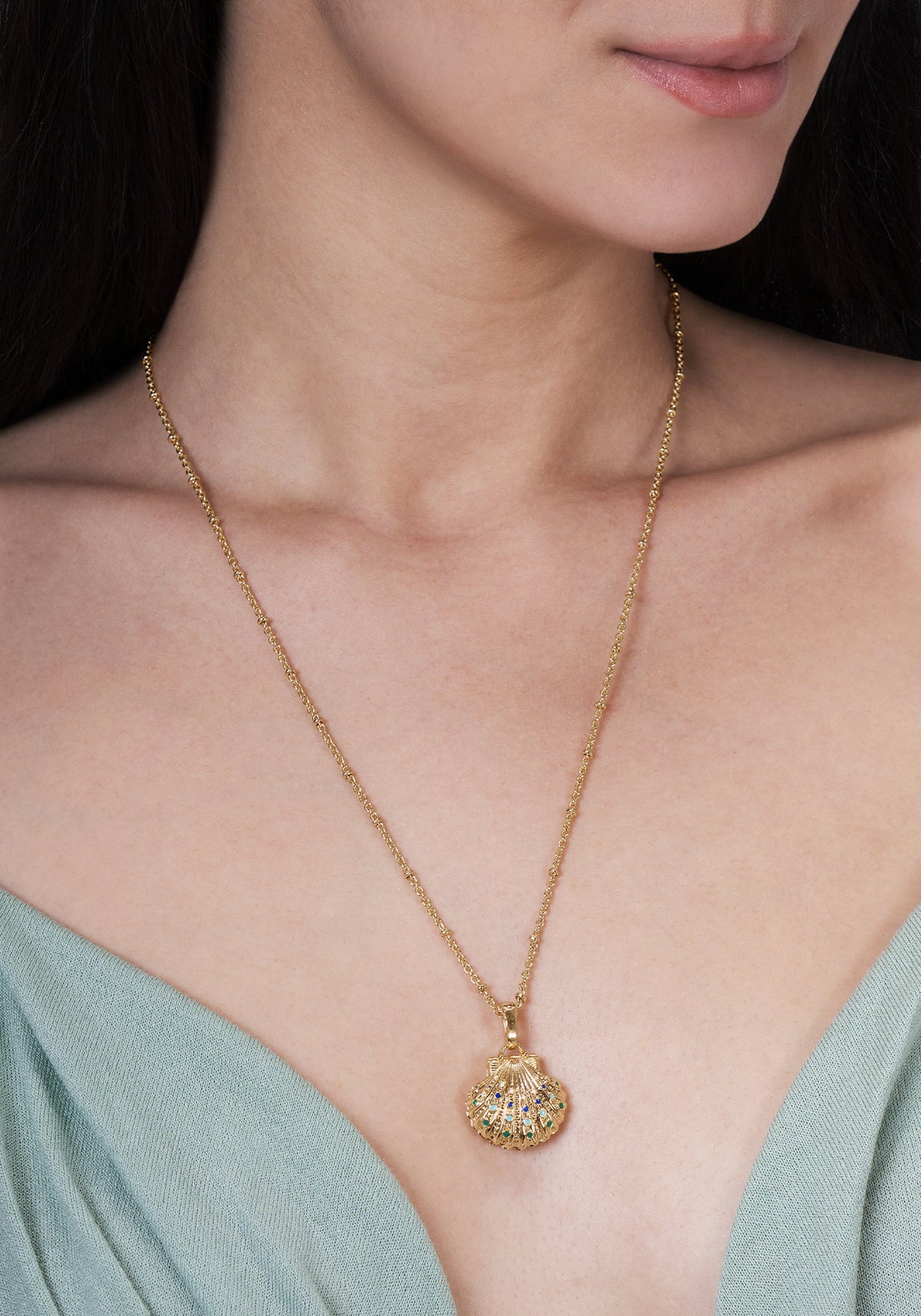 Anabel Aram Milos Shell Locket Charm, a gold-plated shell locket necklace on a chain featuring small, colorful gemstone accents.