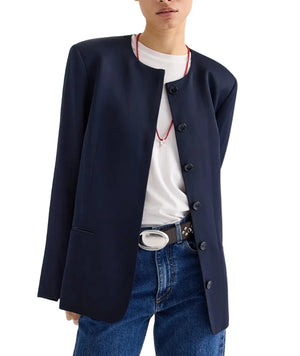 A person wears the TWP Cecelia Coated Viscose Linen Jacket in navy blue over a white t-shirt, blue jeans, a black belt with a silver buckle, and a red necklace.