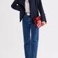 A person wearing the TWP Cecelia Coated Viscose Linen Jacket, styled with a white t-shirt, blue jeans, sandals, and holding a large red clutch bag.