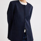 Model wears the TWP Cecelia Coated Viscose Linen Jacket—collarless, navy, with an elongated silhouette—layered over a white t-shirt and blue jeans, set against a plain light background.