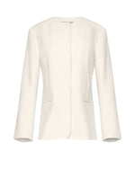 The TWP Cecelia Jacket is a women's long-sleeve, off-white blazer made from 100% linen. It features a collarless design and no visible buttons, showcased on a white background.