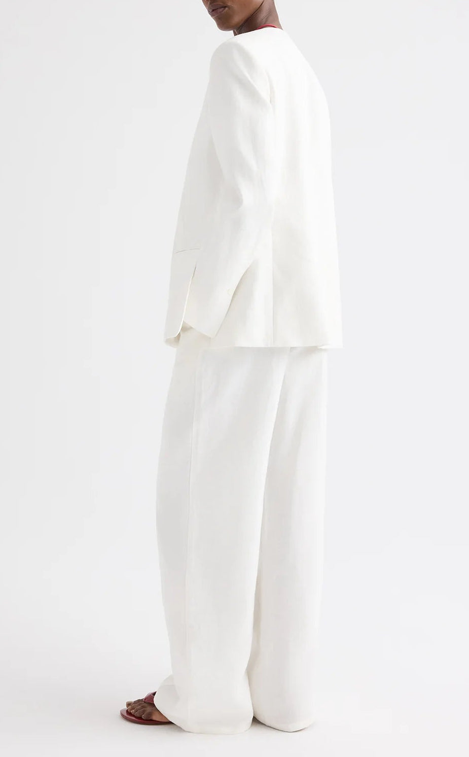 A person wearing the TWP Cecelia Linen Jacket—an ivory washed linen, collarless blazer—paired with wide-leg trousers, stands against a plain white background, facing away from the camera.