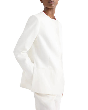 Wearing the TWP Cecelia Linen Jacket and matching white pants in ivory washed linen, this person faces slightly to the side with one hand in a pocket, creating an elongated silhouette.