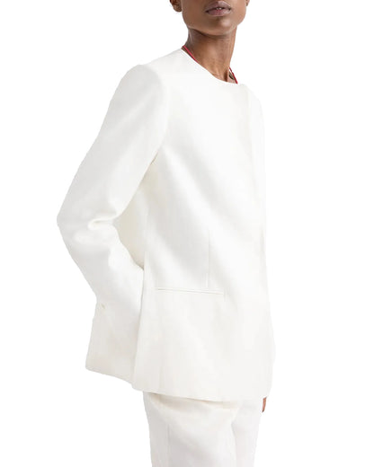 Wearing the TWP Cecelia Linen Jacket and matching white pants in ivory washed linen, this person faces slightly to the side with one hand in a pocket, creating an elongated silhouette.