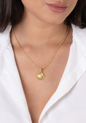 A woman wears a white blouse and the Anabel Aram Scallop Shell Charm, an 18k gold plated necklace.