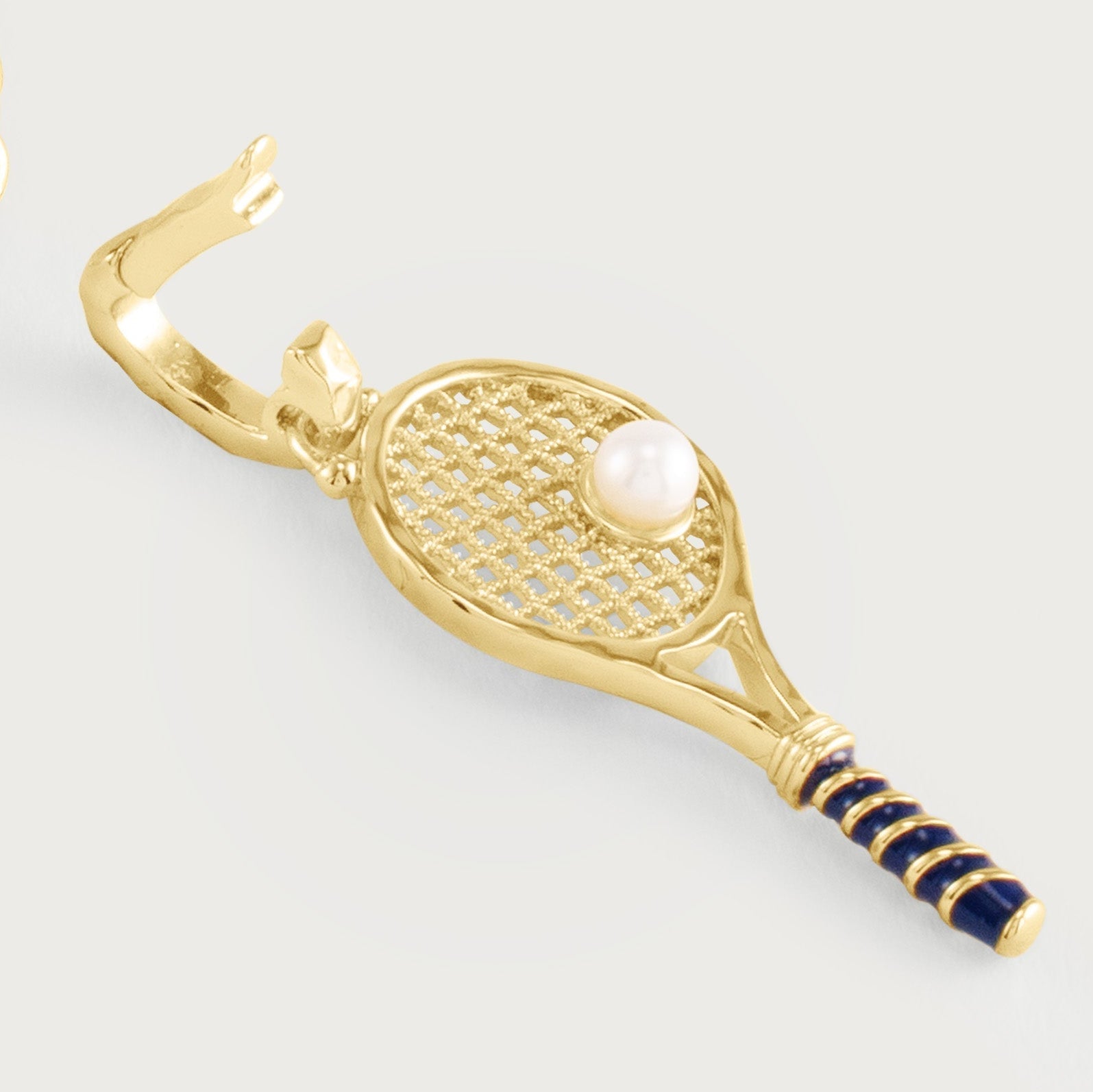 The Anabel Aram Tennis Racket Charm is a gold-plated earring with blue enamel on the handle and a pearl accent as the ball.