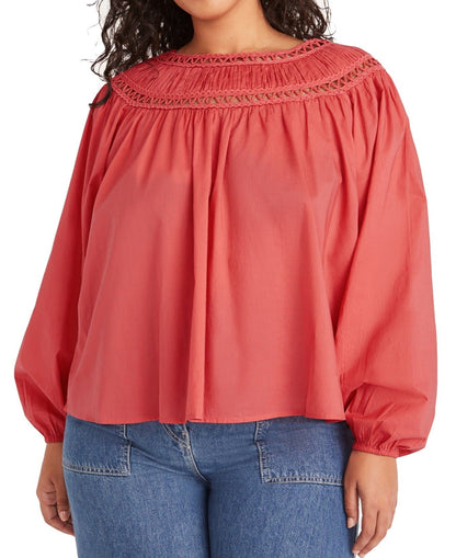 Person wearing the Merlette New York Merlette Ardent Top, a long-sleeve coral blouse with voluminous sleeves and intricate handcrafted soutache trim near the neckline, paired with blue jeans.