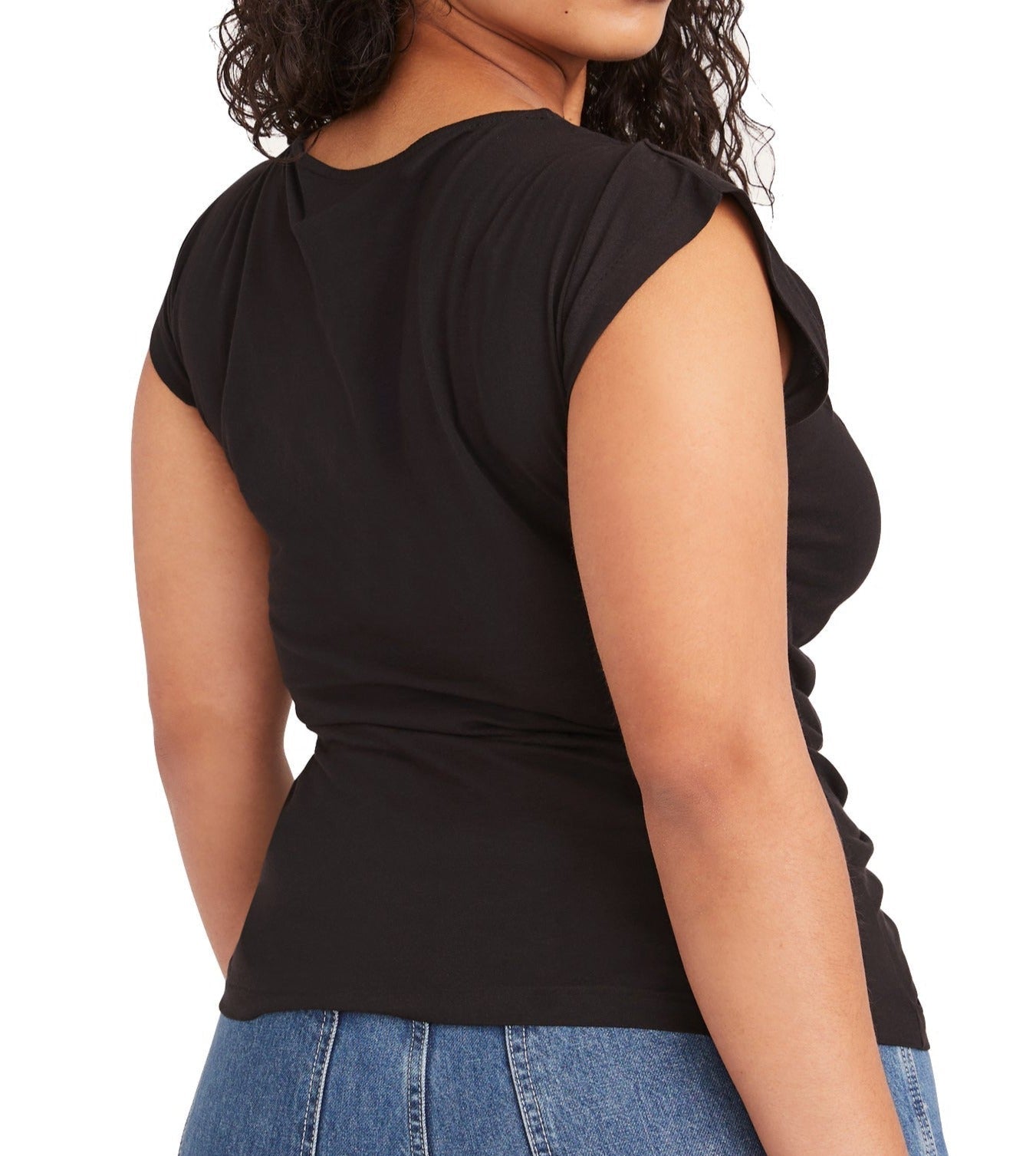 A woman wearing a Merlette New York Merlette Reverie Jersey Top in black and blue jeans viewed from a side angle.