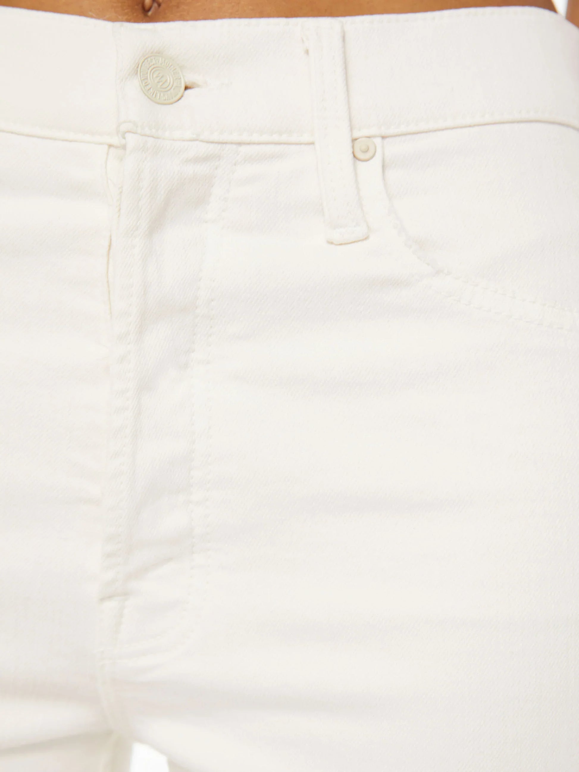 Close-up of a person wearing the Mother Denim The Tomcat Ankle pants by Mother in an off-white wash, highlighting the button, zipper, and front pockets.