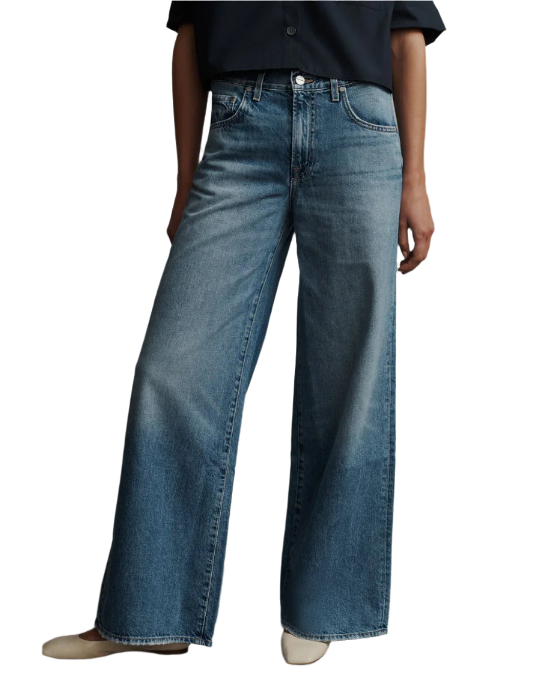 Dressed in TWP Tiny Dancer Jeans and a dark top, a person poses elegantly against a plain background, capturing the essence of vintage style.
