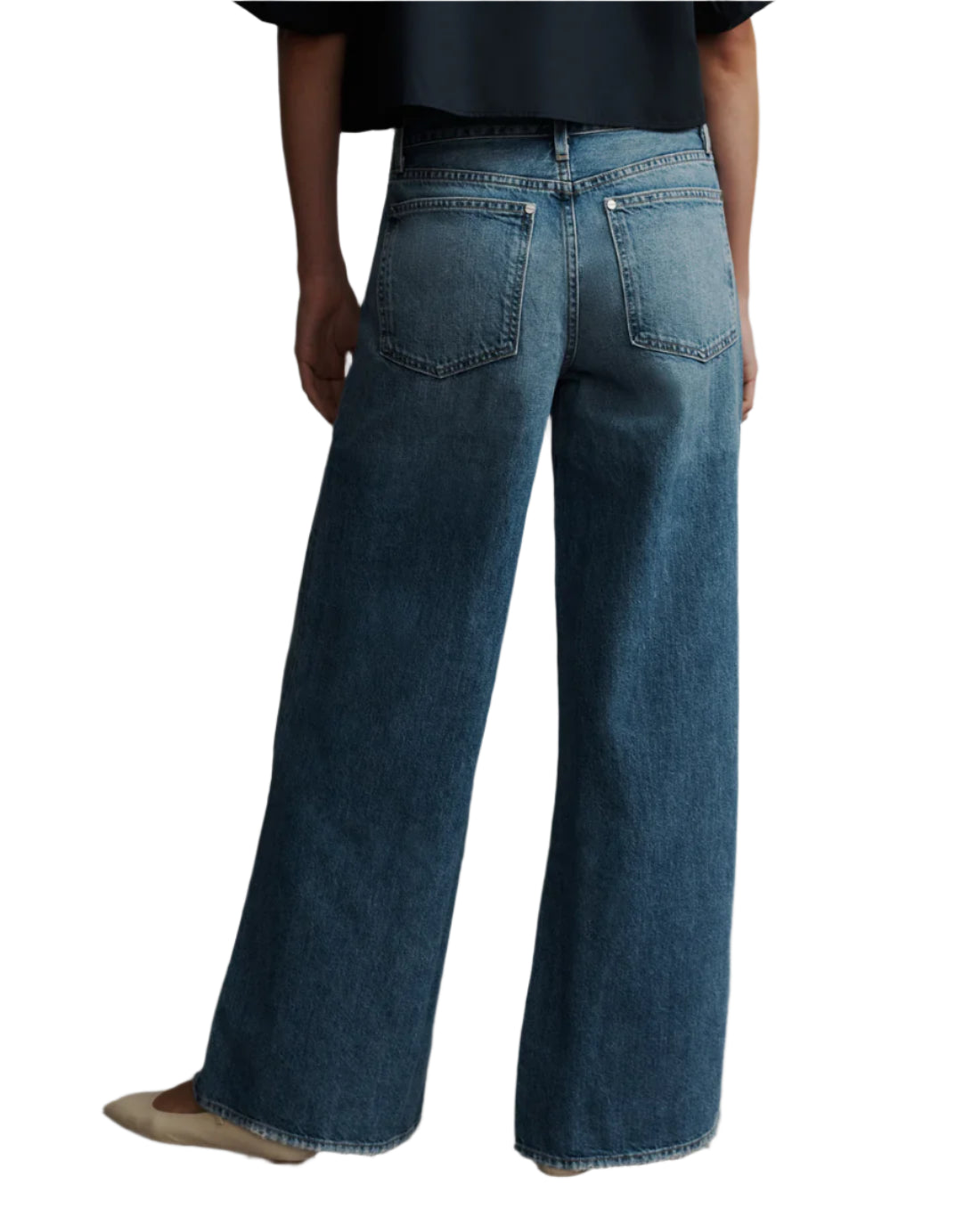 A person is seen from behind wearing TWP's Tiny Dancer Jeans, vintage-inspired wide-leg denim, paired with beige shoes.