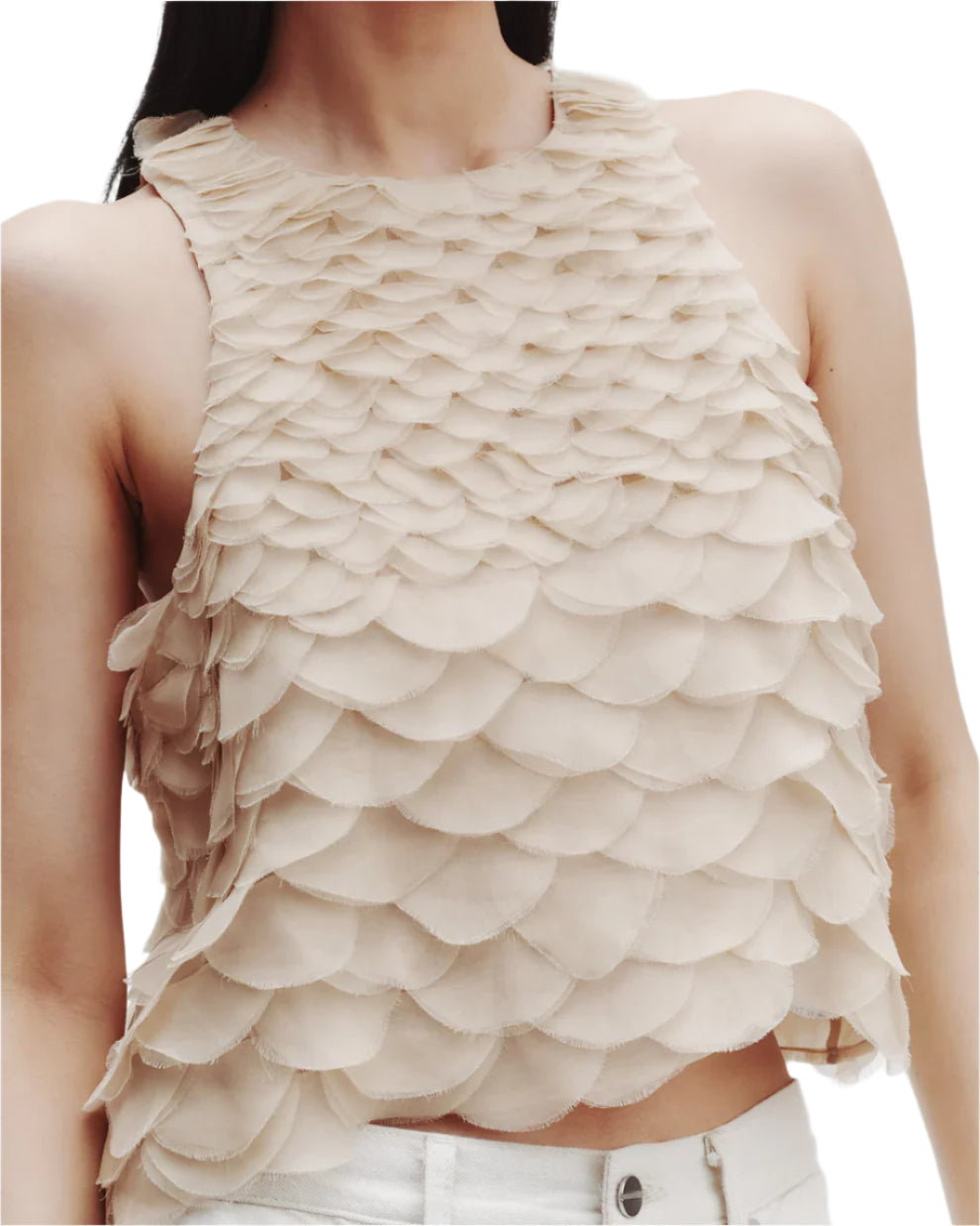 A woman in TWP's Shell Silk Organza Fishscales Top—a beige, elegant sleeveless crop crafted from silk organza with hand-sewn scallops—styled chicly with white pants.
