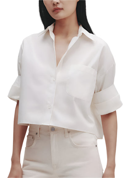 The woman wears the TWP Next Ex Shirt, a white short-sleeve button-up made of superfine Italian cotton with a front pocket. Paired with high-waisted pants, she exudes effortless elegance.