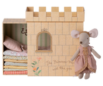 A Maileg Princess and the Pea Mouse dressed as a princess standing beside a cardboard castle playset with a stack of patterned mattresses inside, inspired by the fairy tale "The Princess and the Pea.