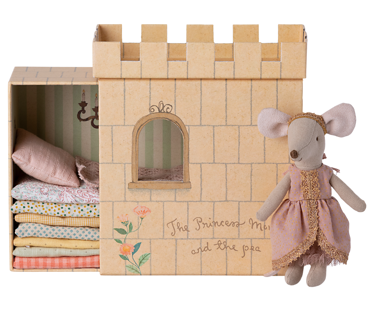 A Maileg Princess and the Pea Mouse dressed as a princess standing beside a cardboard castle playset with a stack of patterned mattresses inside, inspired by the fairy tale "The Princess and the Pea.