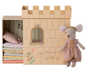 A Maileg Princess and the Pea Mouse dressed as a princess standing beside a cardboard castle playset with a stack of patterned mattresses inside, inspired by the fairy tale "The Princess and the Pea.