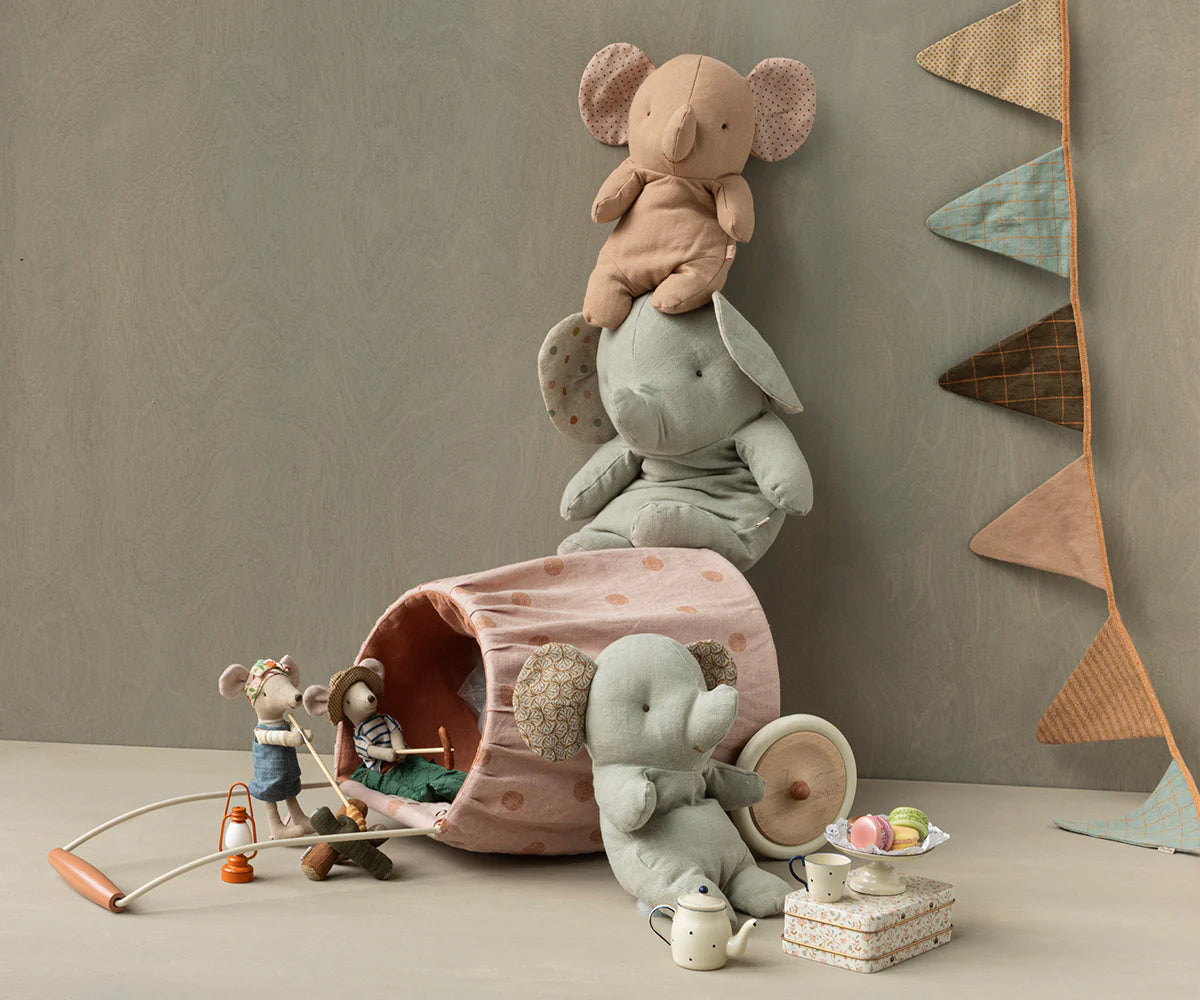 Three Maileg Hiker Mouse, Big Brother dolls are arranged with plush elephants, a fabric basket, assorted toys, and a tea set on a neutral background, complemented by a decorative pennant banner on the wall.