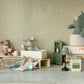 Four Maileg mice, including the Big Sister Mouse in Matchbox - Pyjamas, are arranged in a dollhouse scene with miniature furniture; a plush rhino sits in a mug on stacked books in the background.