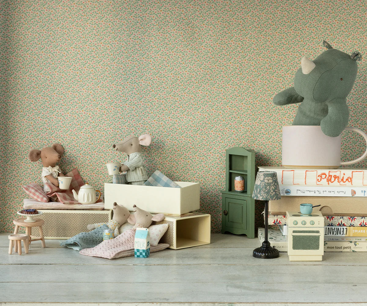 Four Maileg mice, including the Big Sister Mouse in Matchbox - Pyjamas, are arranged in a dollhouse scene with miniature furniture; a plush rhino sits in a mug on stacked books in the background.