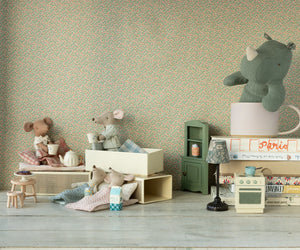 Four Maileg mice, including the Big Sister Mouse in Matchbox - Pyjamas, are arranged in a dollhouse scene with miniature furniture; a plush rhino sits in a mug on stacked books in the background.