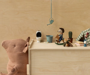 A large brown teddy bear in a cowboy hat leans against wood beside Maileg's Cowboy Mouse on Rocking Horse, Little Brother, plus mini toy items like a tent, cactus, toilet, blue bucket, watering can, and other figurines.