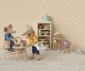 Maileg’s Dad Mouse enjoys tea and pastries at a small table with mouse furniture, surrounded by shelves of baked goods and baking supplies in a cozy miniature kitchen scene.
