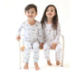 Two smiling children sit on a wooden bench, holding hands and wearing matching Angel Dear Baby and Kids' Golf Carts Long Sleeve Loungewear Sets, crafted from breathable fabric for cozy, all-day comfort.