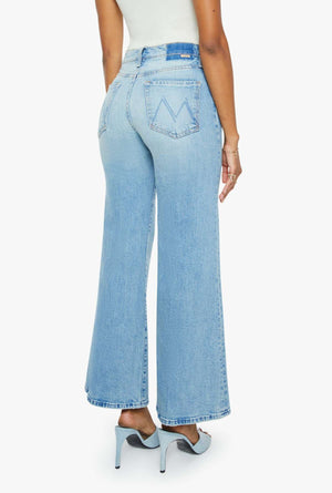 Someone shown from the back wears Mother’s The Tomcat Roller high-waisted wide-leg jeans in light blue with matching light blue high-heeled shoes.