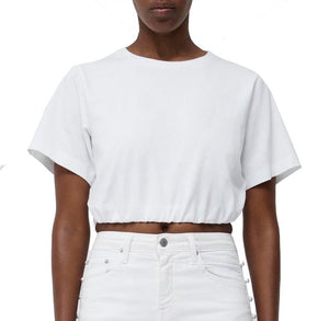 A person wearing the Simkhai Jojo Cropped T Shirt paired with white high-waisted pants, showcasing a modern style against a plain background. The outfit's versatile design and relaxed fit make it perfect for any casual occasion.