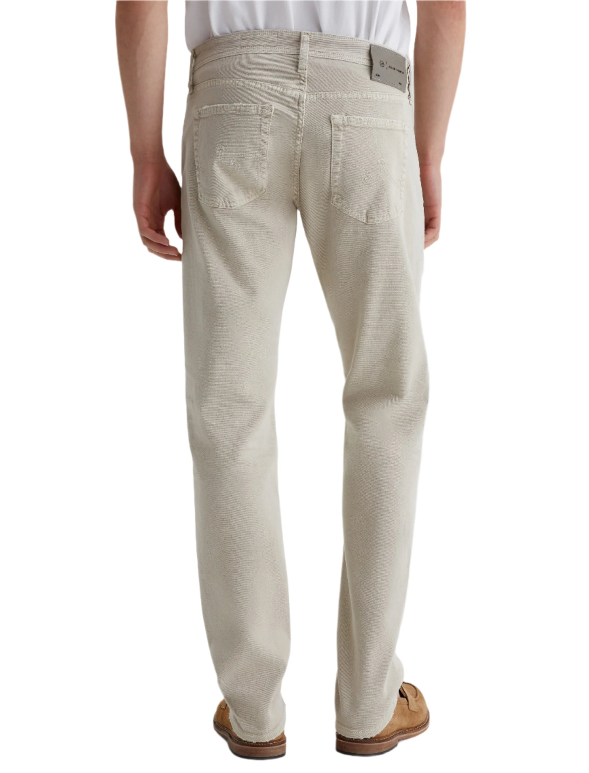 A person wearing AG Jeans Tellis AG-ed™ Modern Slim Denim in light beige and brown shoes, standing with their back to the camera.