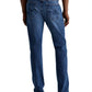 A person is shown from the back wearing AG Jeans Tellis Modern Slim Denim in medium blue, paired with a white shirt and brown shoes.
