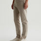 A person wearing AG Jeans Tellis Sueded Sateen Jeans in beige and white sneakers stands against a plain light background.