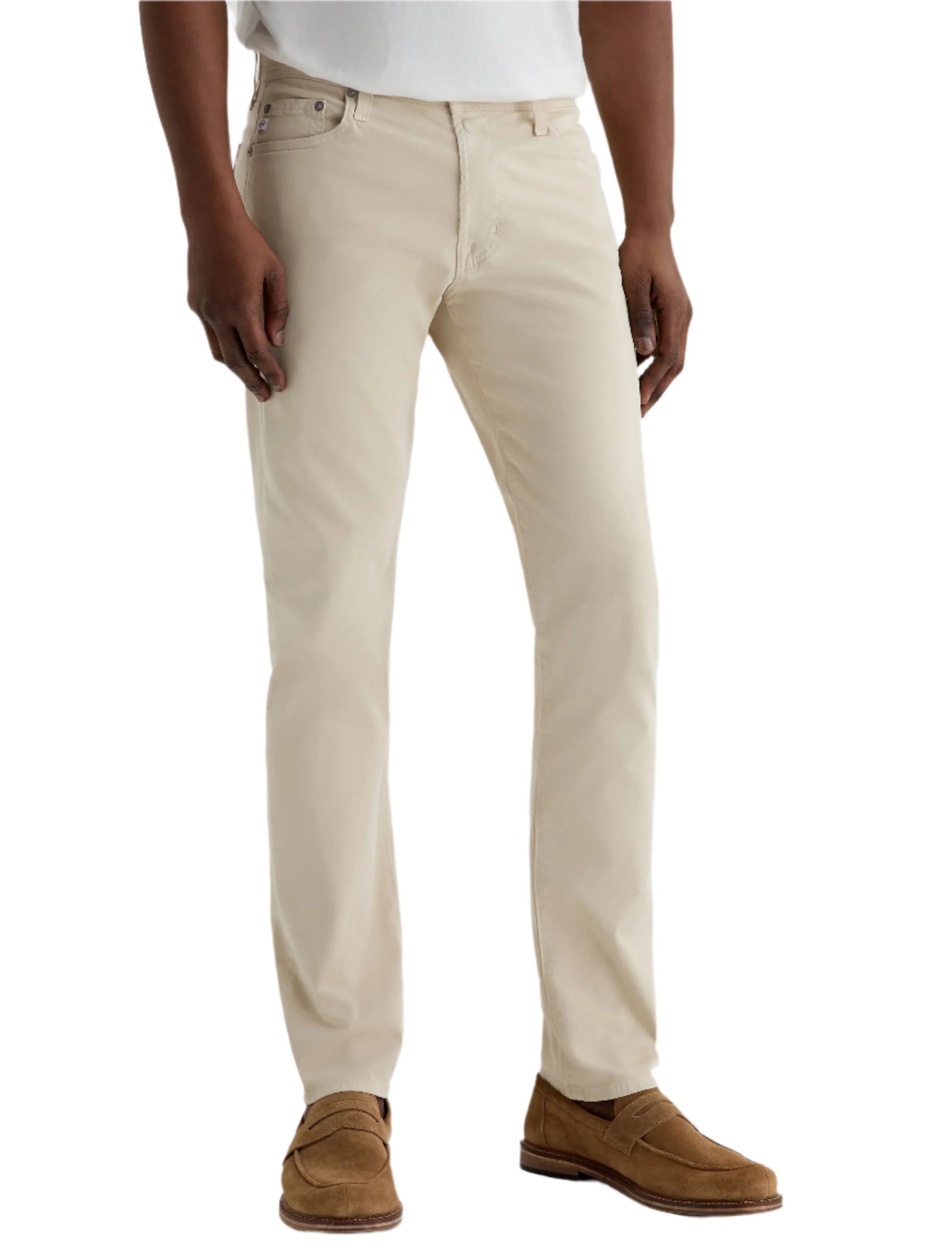 A person wearing AG Jeans Tellis Modern Slim Sueded Stretch Sateen pants, paired with a white shirt and light brown suede loafers, stands against a plain light background.