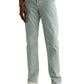 A person stands with one hand in their pocket, wearing AG Jeans Tellis Modern Slim Sueded Stretch Sateen light green men's pants, paired with a white shirt and white sneakers against a plain background.