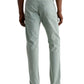 A person wearing AG Jeans' Tellis Modern Slim Sueded Stretch Sateen in light green, a white t-shirt, and white sneakers stands with their back to the camera against a plain background.