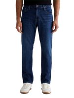 A person wearing AG Jeans Everett in Denim Crusade and white sneakers, captured from the waist down against a plain background.