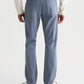 A man is shown from the back against a plain background wearing AG Jeans’ Everett 7 Years Sulfur slim straight grey-blue jeans, paired with a white long-sleeve shirt and white sneakers.