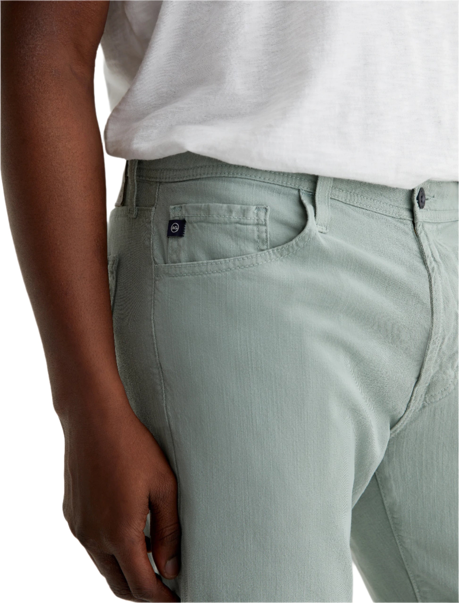 A person wearing AG Jeans Everett Slim Straight Leg cotton-linen twill men's pants in light green and a white shirt, with their left hand resting by their side.