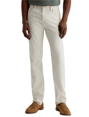 A person wearing AG Jeans Everett Slim Straight Leg men's pants, a green shirt, and brown suede loafers, standing on a white background.