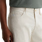 A person is shown from waist to mid-thigh wearing AG Jeans' Everett Slim Straight Leg in off-white and a green textured shirt, with one hand relaxed by their side.