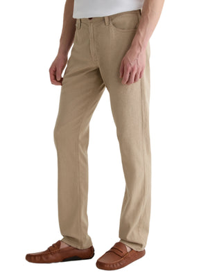 A person wears AG Jeans' Everett Slim Straight beige jeans with a mid-rise waist, paired with a white shirt and brown loafers, standing against a white background.
