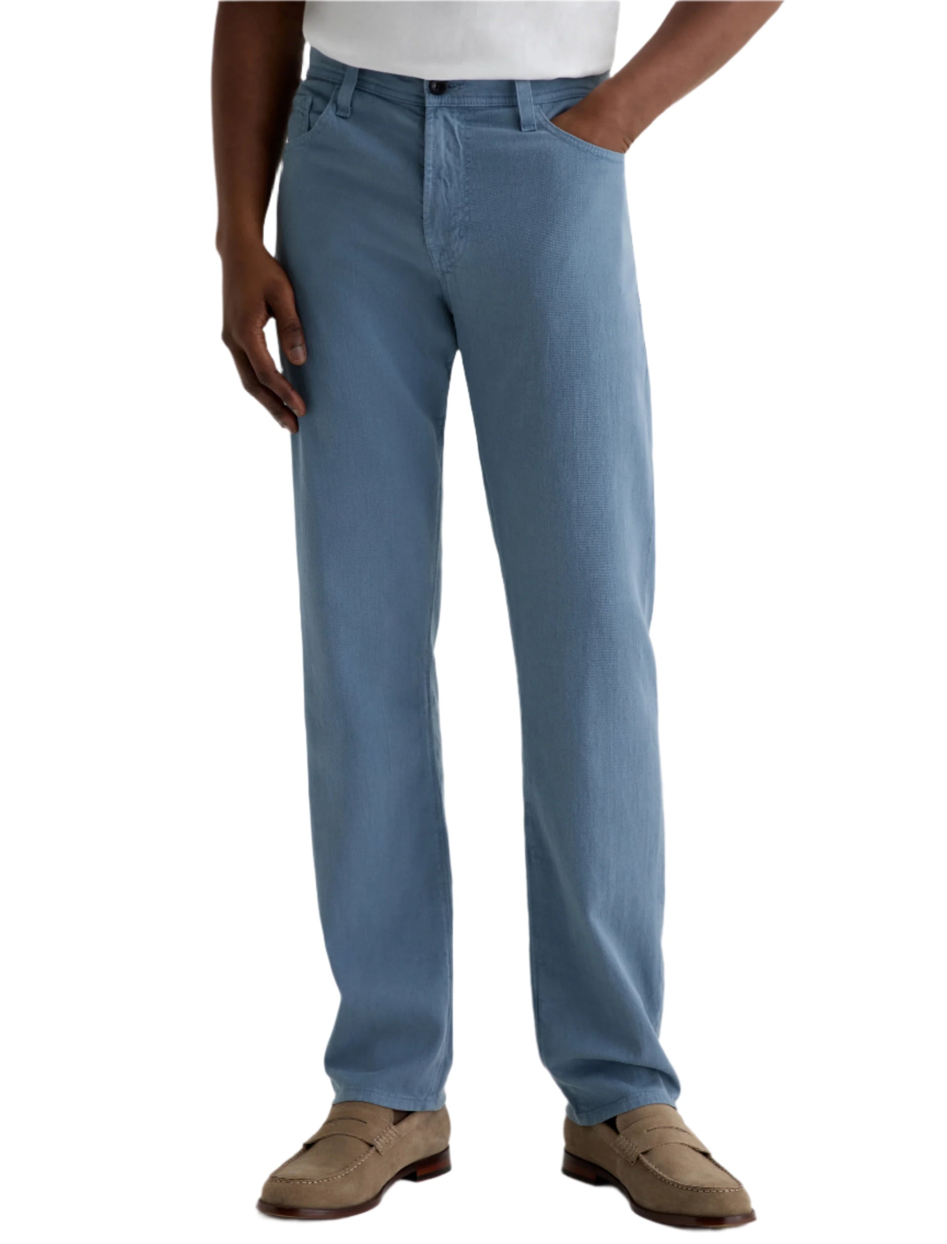 A person wearing AG Jeans Everett Slim Straight with a classic five-pocket design, a white shirt, and tan loafers stands with one hand in their pocket against a plain background.