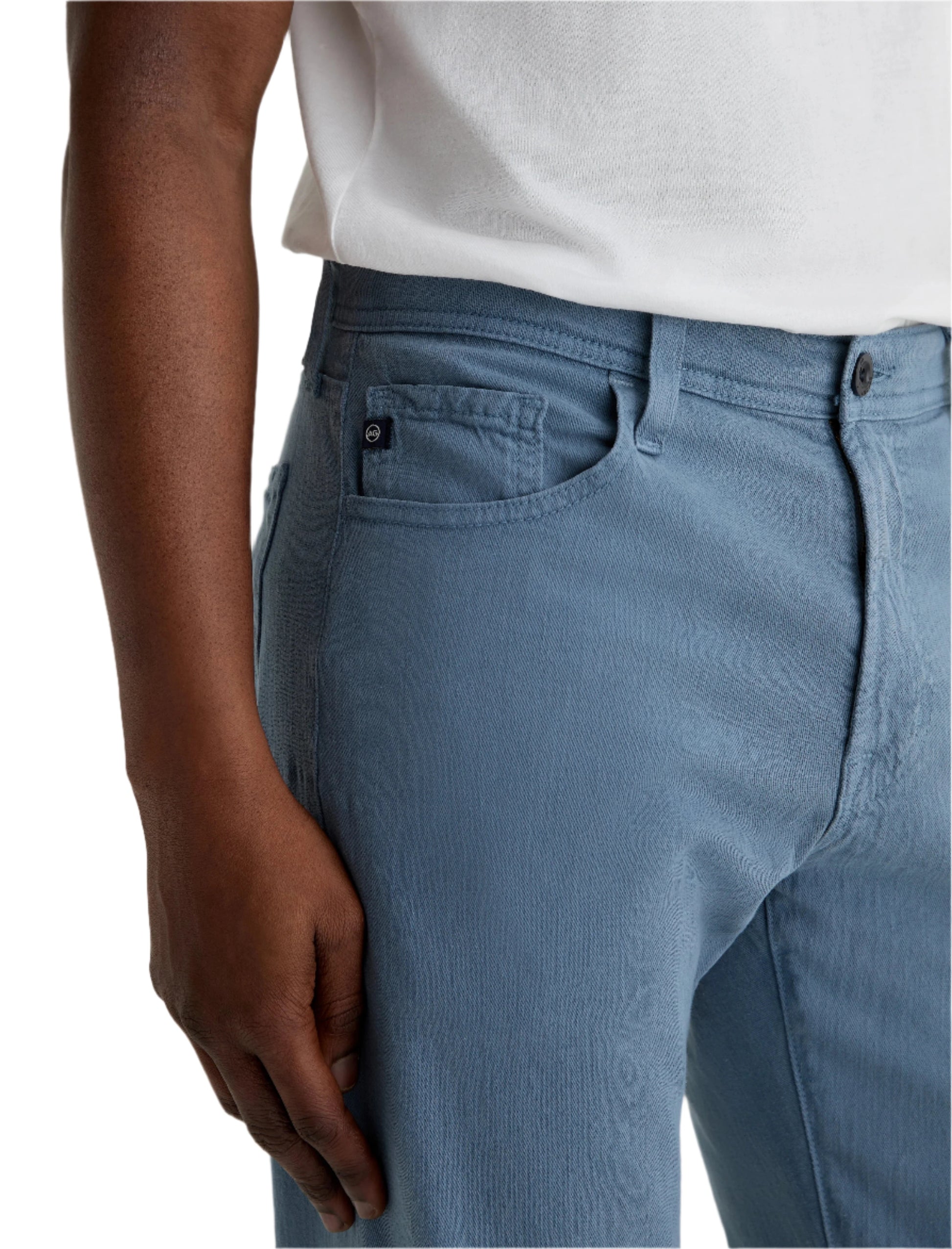 A person wearing AG Jeans' Everett Slim Straight jeans in a light blue wash with a mid-rise waist and five-pocket design, paired with a white shirt, shown from mid-torso to knee, one hand resting by their side.