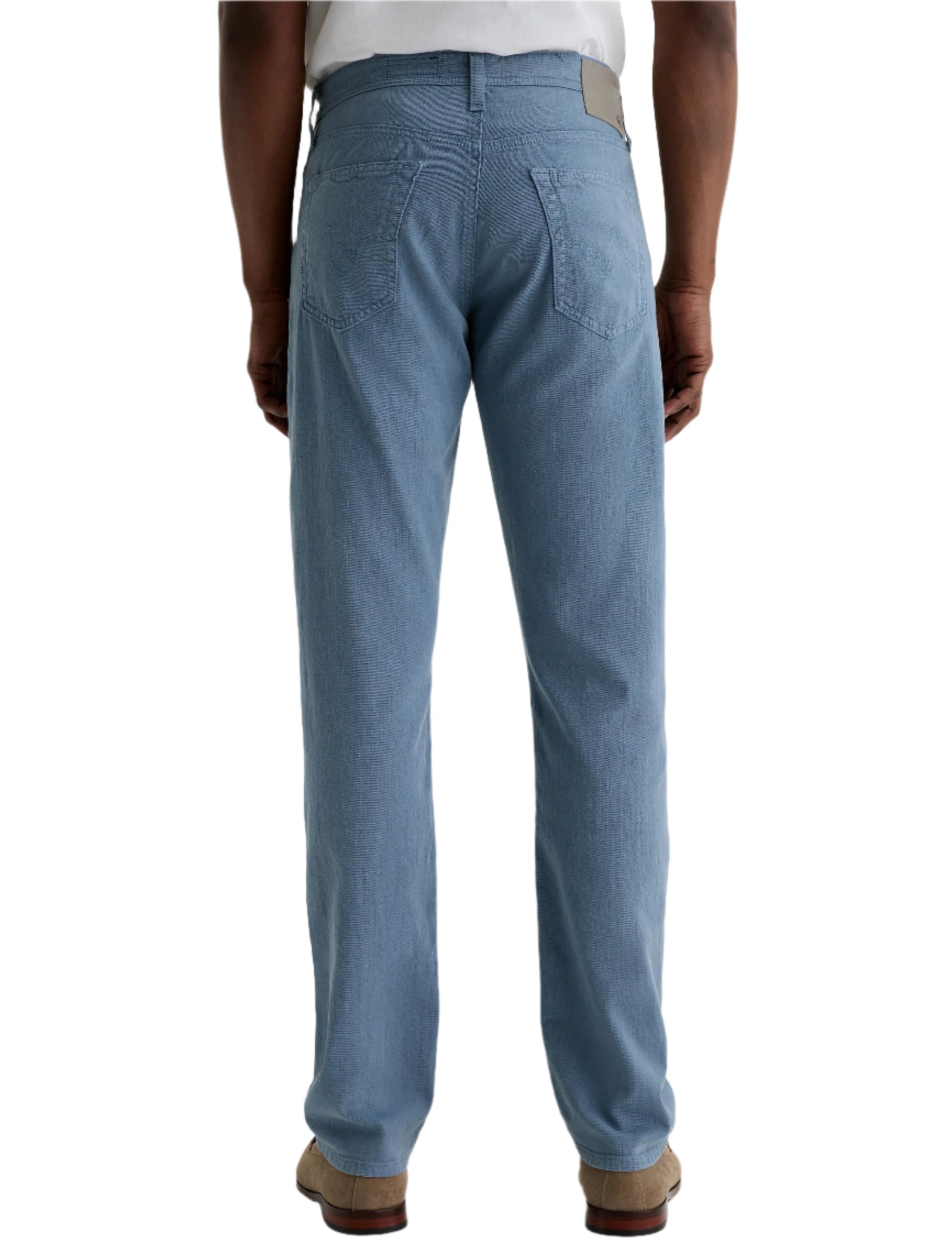 A person stands facing away, wearing AG Jeans Everett Slim Straight with a mid-rise waist, paired with a white shirt and beige shoes against a plain background.