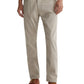 A person wearing AG Jeans' Everett Sueded Slim Straight jeans in light beige with a mid-rise waist, paired with a white shirt and brown leather shoes, is shown from shoulders to feet against a plain background.