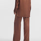 A person wearing a brown silk satin long-sleeve shirt and CO Elastic Silk Pant by CO, viewed from the back against a plain white background.